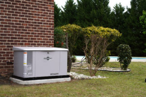 Generator on the wall of a red brick house. Bushes and in ground pool visible in the back.